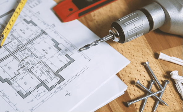 Blueprints, a drill and screws on a workbench